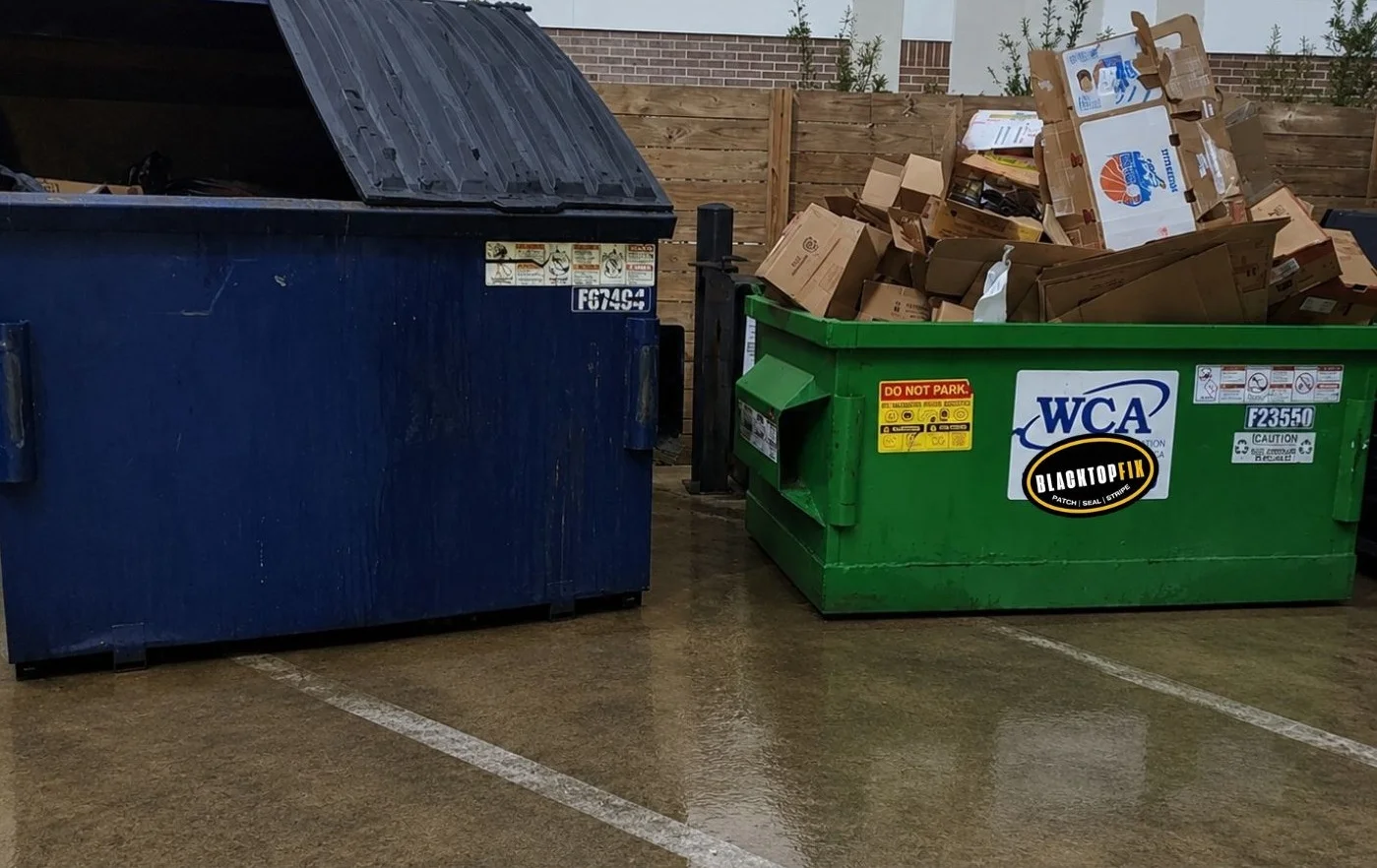 Professional commercial concrete pressure washing service showing a freshly cleaned wet dumpster pad with debris removed, bright parking lot striping, and clean concrete surrounding trash and recycling dumpsters.